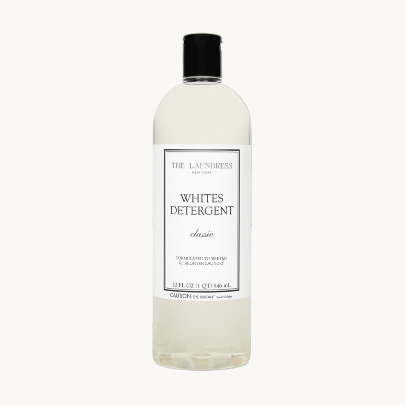 The Laundress Whites Detergent formulated to whiten & brighten laundry laying in water with white fabric.